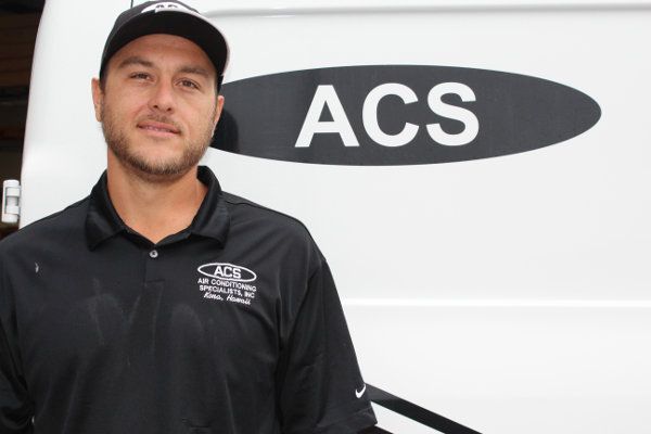 A man in a black ACS company polo and hat stands in front of a white van with an ACS logo.