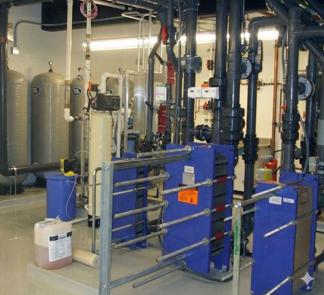 Industrial water treatment system featuring several grey tanks, pipes, and blue plate heat exchangers in a facility.