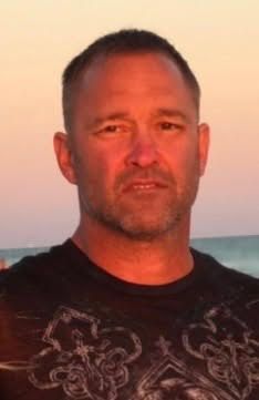 A person with short hair and facial hair outdoors at sunset.