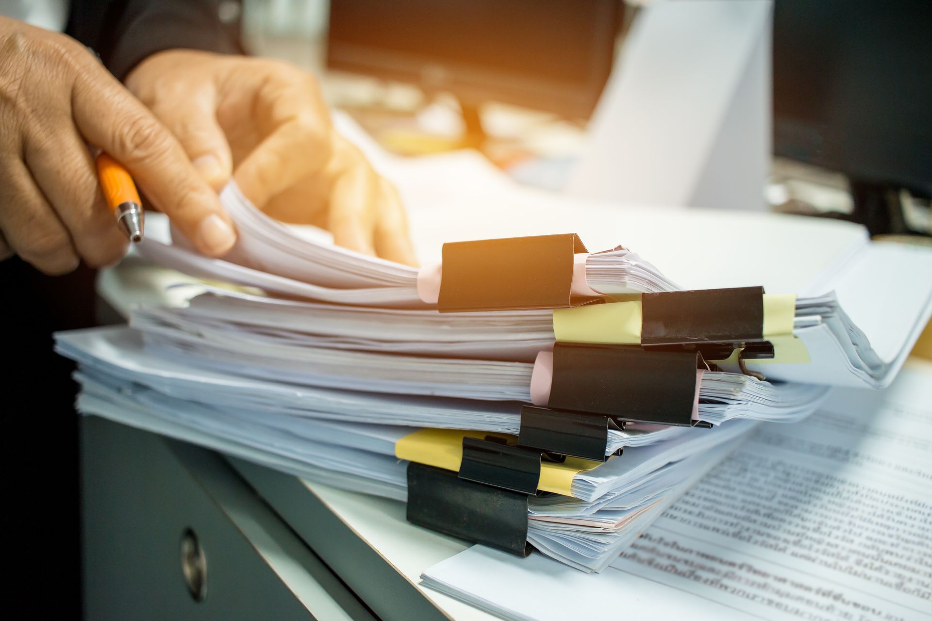 Person with pen examining a stack of papers held together by clips in an office.