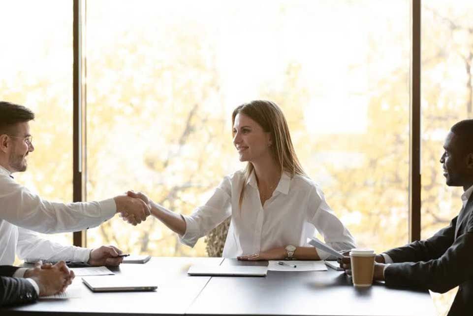 People shaking hands at a table, in a bright office setting.