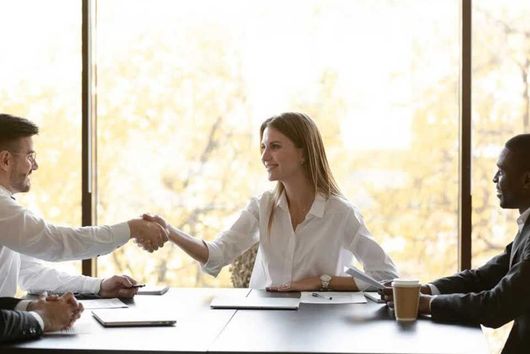 People shaking hands at a table, in a bright office setting.