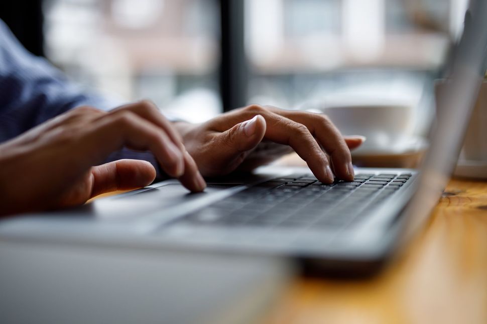 Hands typing on a laptop keyboard at a wooden table near a window.