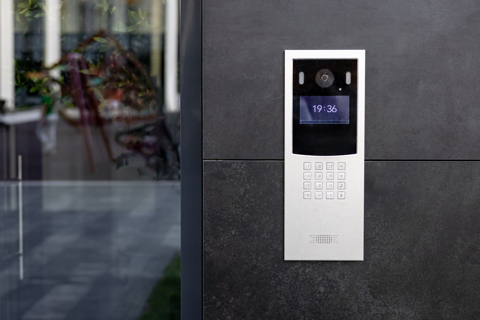 Silver intercom system mounted on a dark gray wall, displaying time.