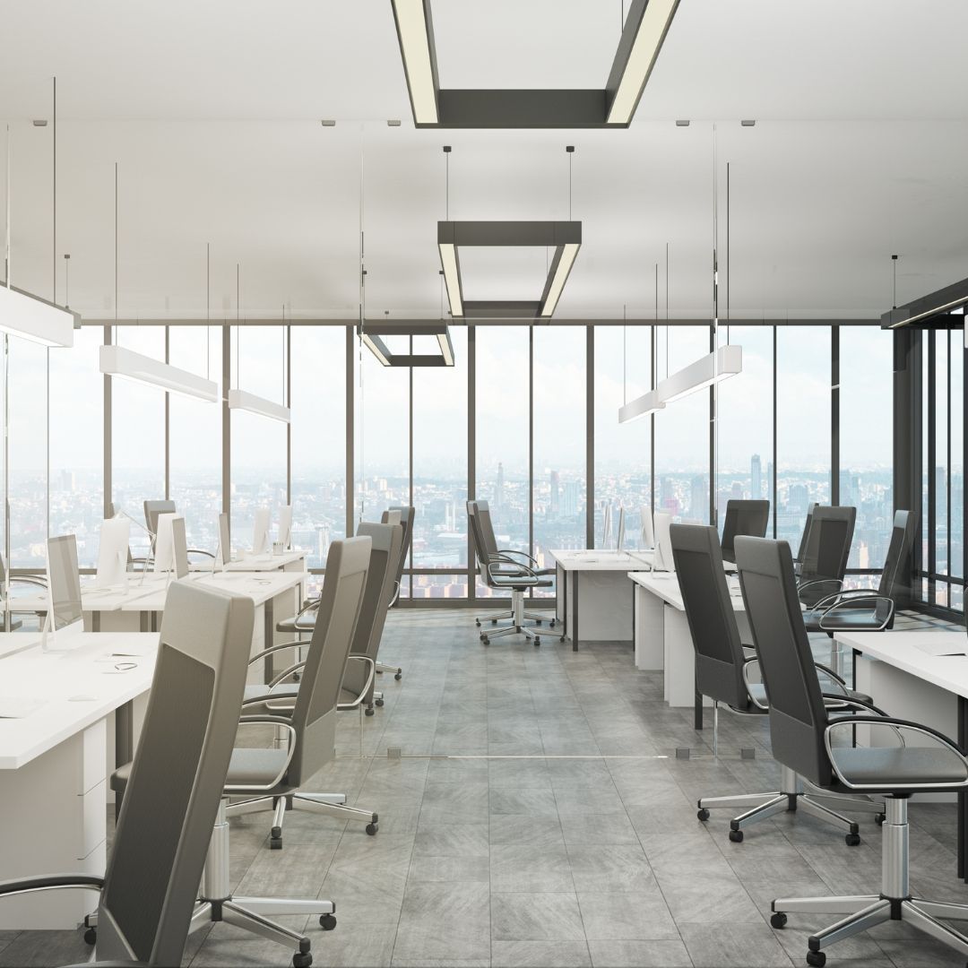 Modern, open-plan office with desks, chairs, and city view through large windows.