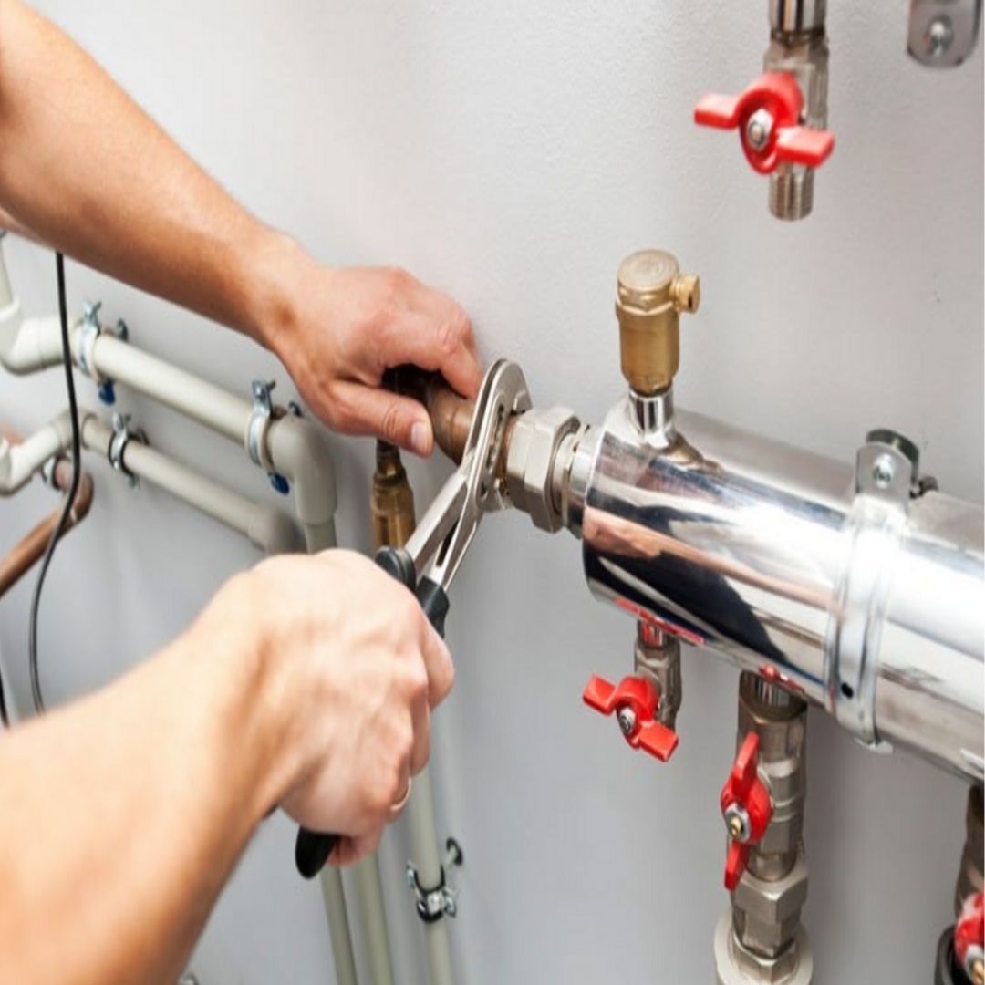A plumber using a wrench on a metal pipe with a white wall background.
