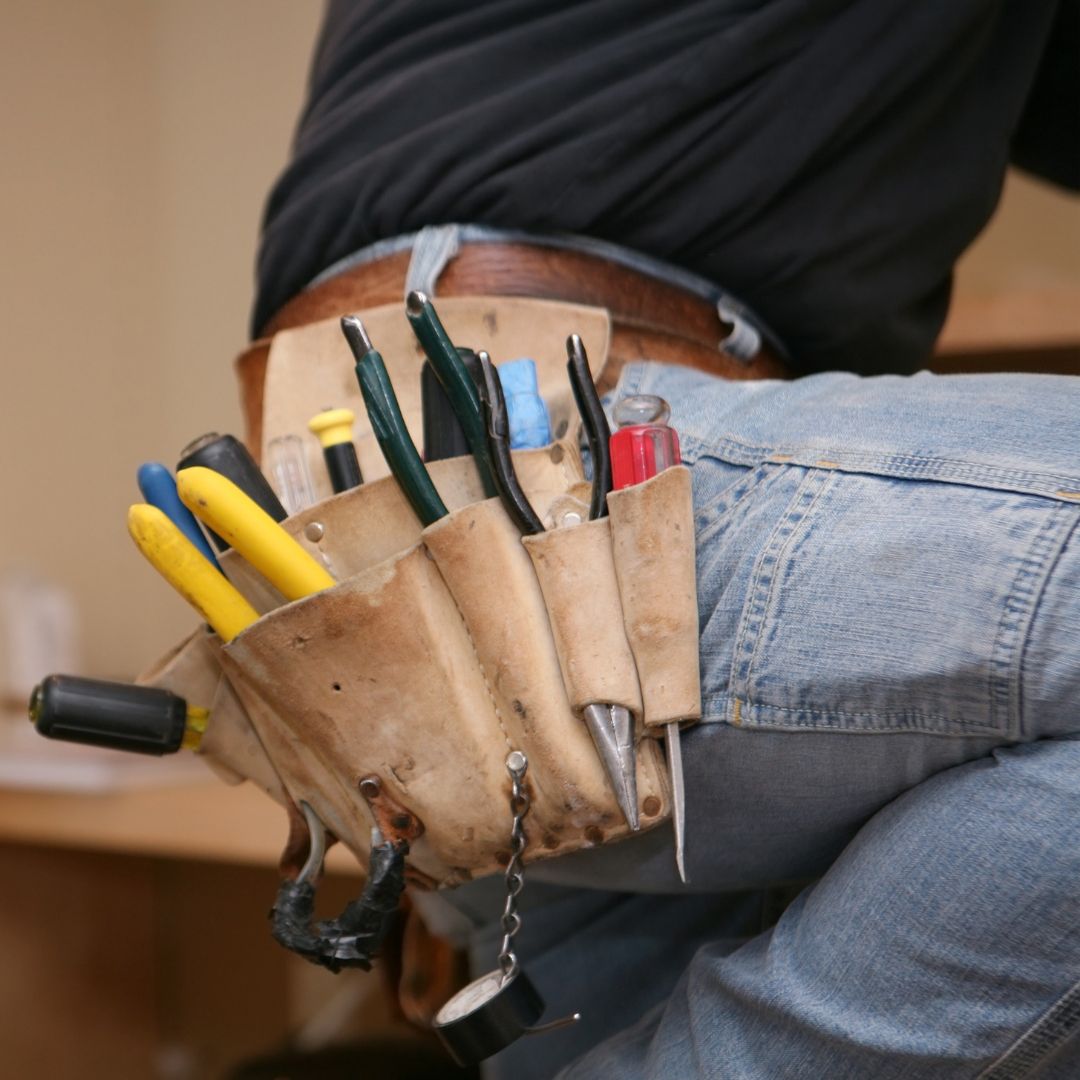 Tool belt on a person wearing jeans, holding various tools.
