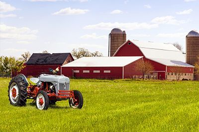An old tractor is parked in a grassy field in front of a barn.