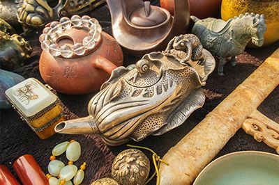 A frog shaped teapot is surrounded by other items on a table.