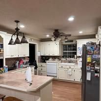 A kitchen with white cabinets , a refrigerator , a stove , a sink , and a ceiling fan.