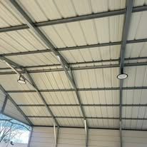 The ceiling of a building with a metal roof and lights hanging from it.