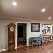 A living room with hardwood floors , a large grandfather clock , a bench , and a picture on the wall.
