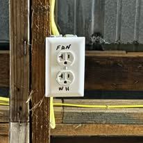 A white electrical outlet on a wooden wall with the words `` fan '' written on it.