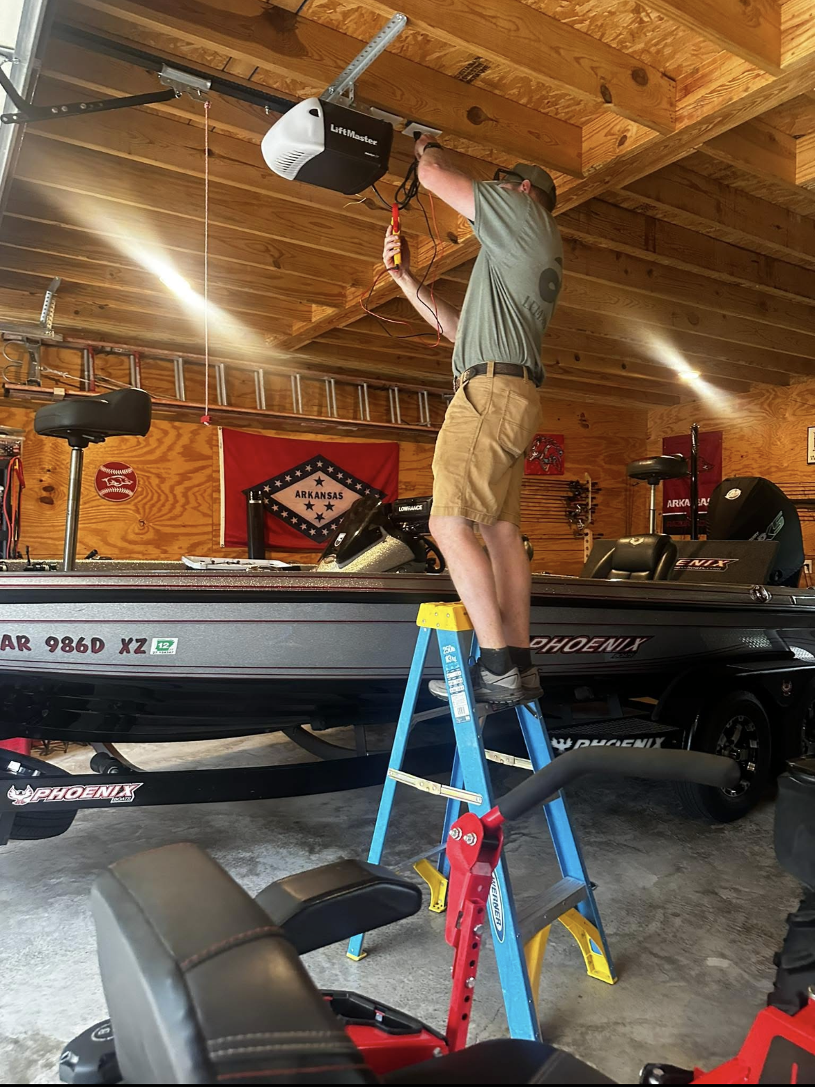 A man is standing on a ladder in a garage working on a garage door opener.