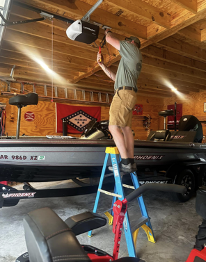 A man is standing on a ladder in a garage next to a boat.