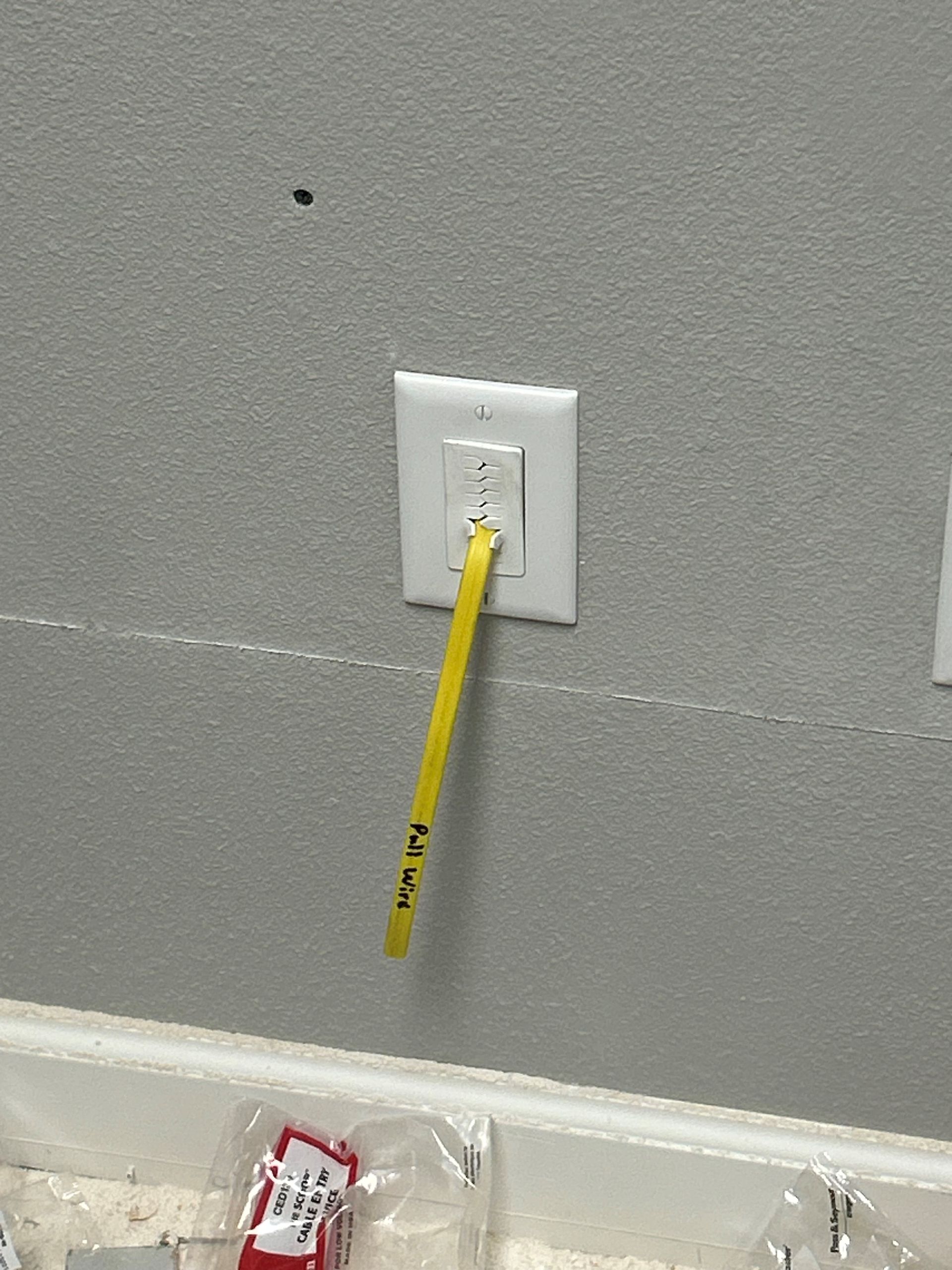 A yellow pencil is plugged into a wall outlet.