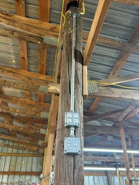 A wooden pole with electrical wires coming out of it in a barn.