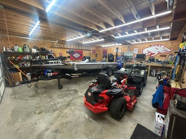 A red lawn mower is parked in a garage next to a boat.