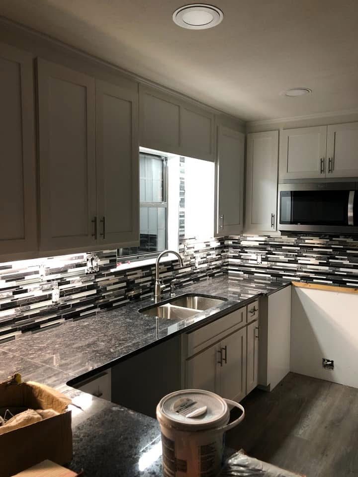 A kitchen with white cabinets , granite counter tops , a sink and a microwave.