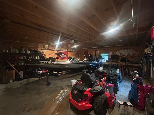 A red lawn mower is parked in a garage next to a boat.