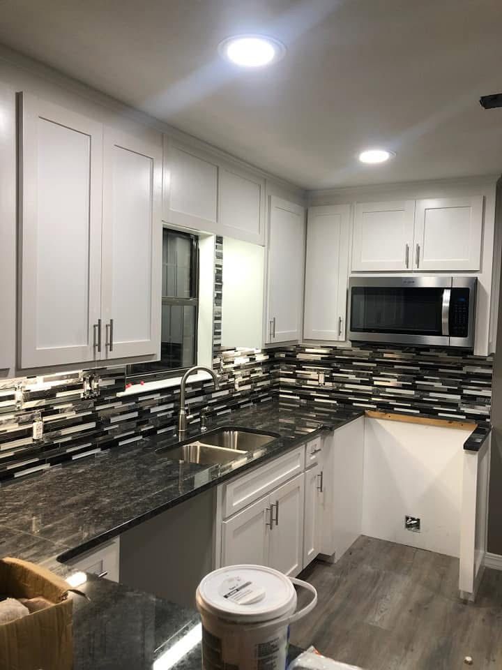 A kitchen with white cabinets , granite counter tops , a sink and a microwave.
