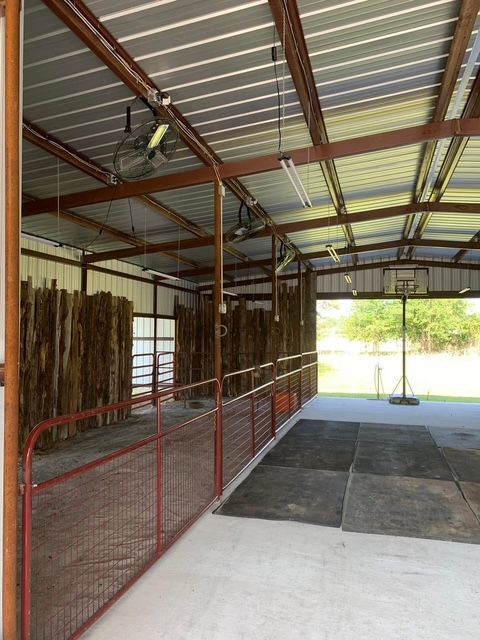 An empty barn with a red fence and fans hanging from the ceiling