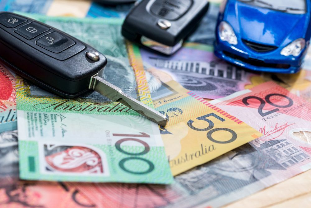 Two car key fobs and a small blue toy car sitting atop Australian 20, 50, and 100 dollar banknotes. — Murwillumbah Motor Wreckers in Gold Coast, NSW