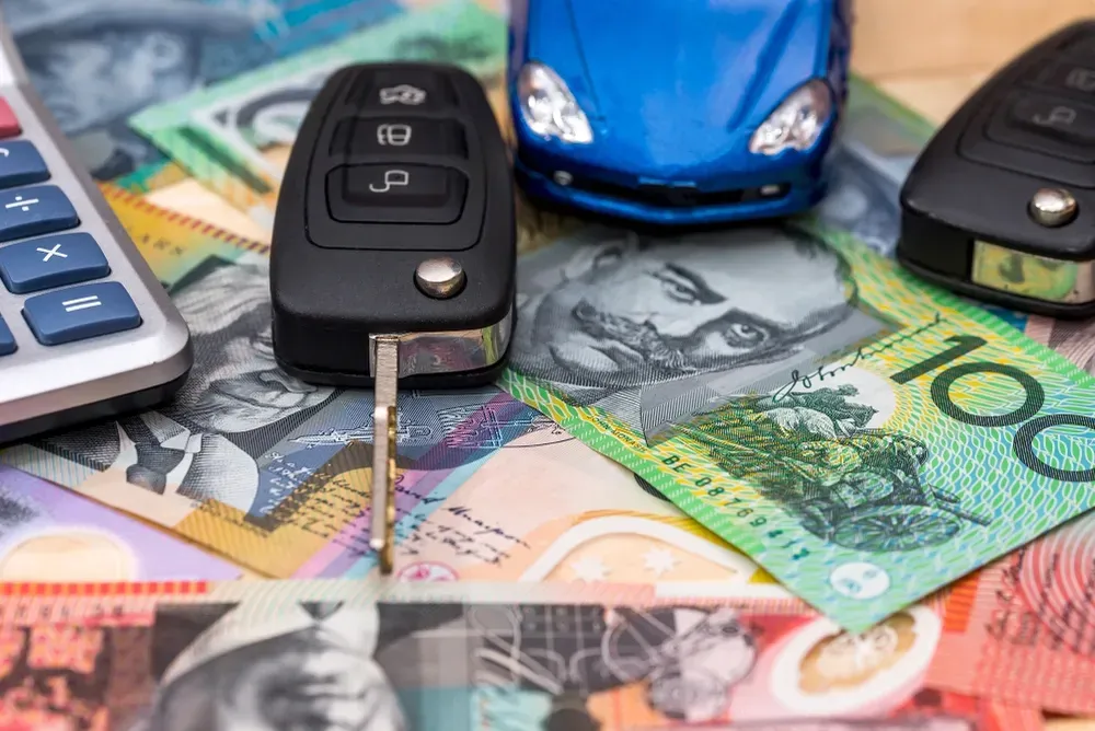 A calculator, two car key fobs, and a blue toy car resting on top of a pile of Australian 100-dollar banknotes. — Murwillumbah Motor Wreckers in Lismore, NSW