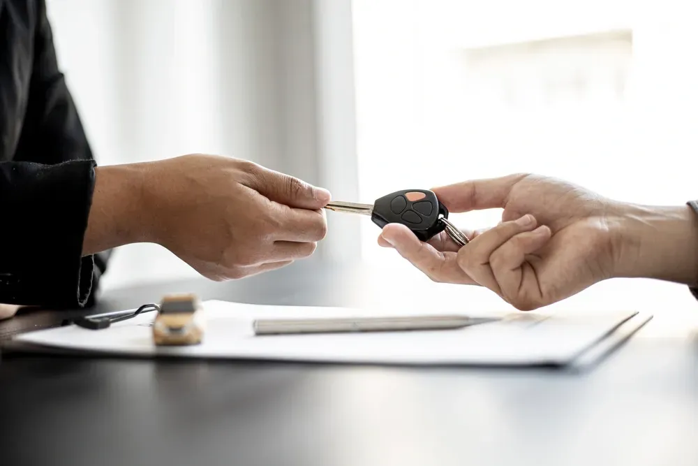 Two people exchange a car key over a contract on a desk, symbolizing a completed vehicle purchase or rental agreement. — Murwillumbah Motor Wreckers in Byron Bay, NSW