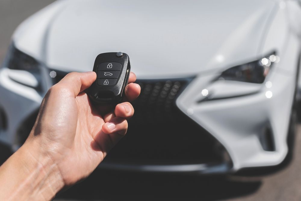 A hand holds a black key fob aimed toward the front of a white Lexus car. — Murwillumbah Motor Wreckers in Gold Coast, NSW