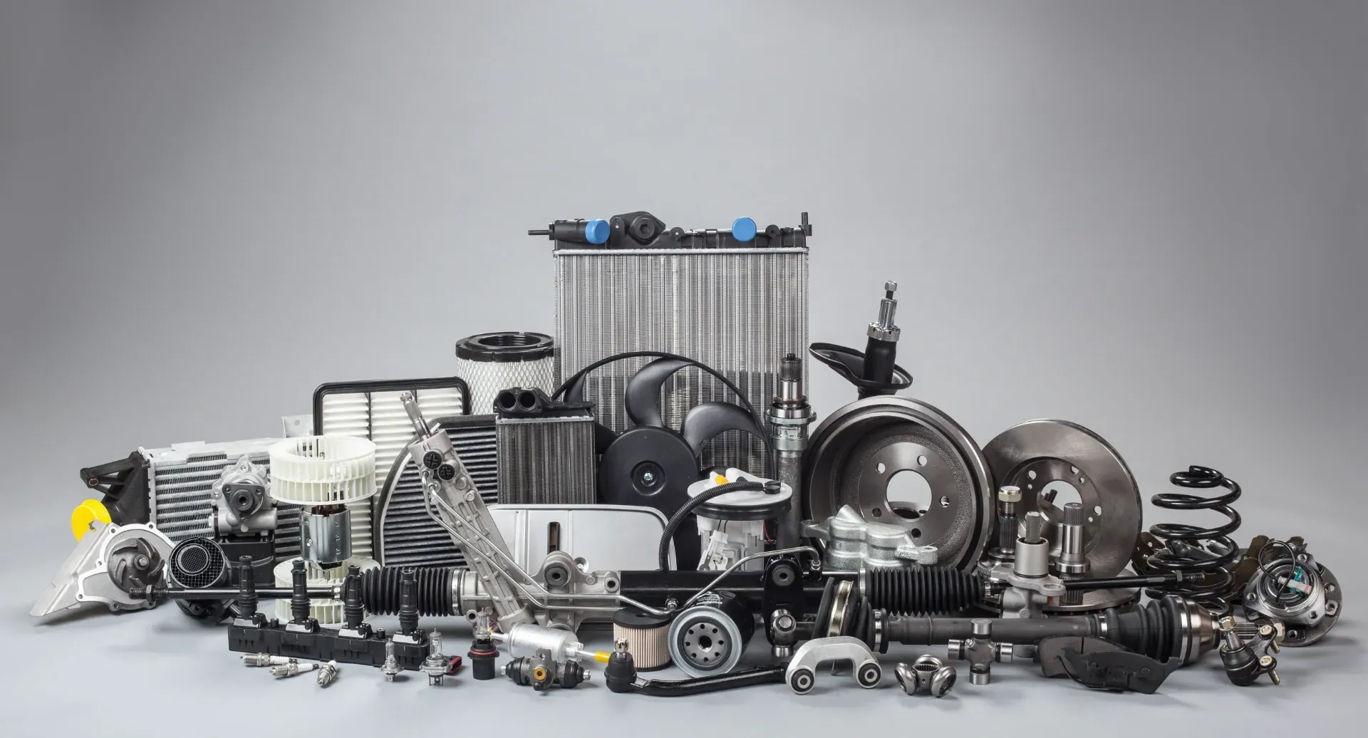 A large pile of various automotive spare parts, including a radiator, brake discs, and filters, on a plain gray background. — Murwillumbah Motor Wreckers in South Murwillumbah, NSW