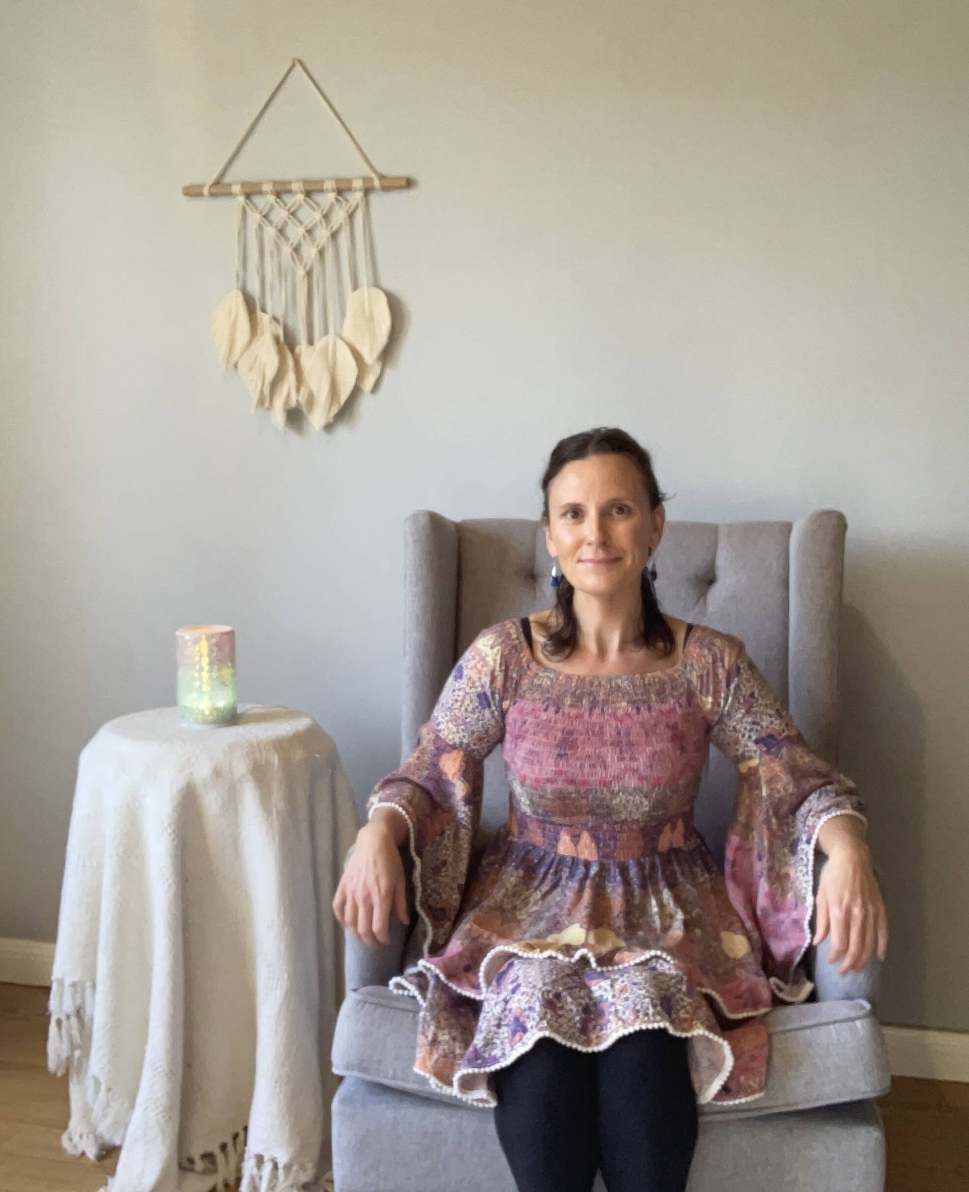 A woman is sitting in a chair in front of a wall hanging.