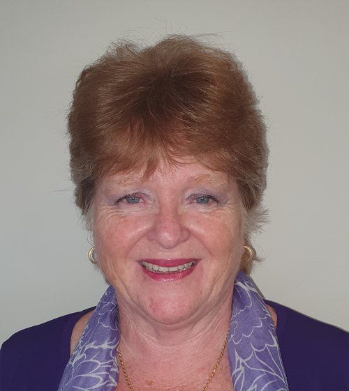 A woman wearing a purple shirt and a purple scarf is smiling for the camera.