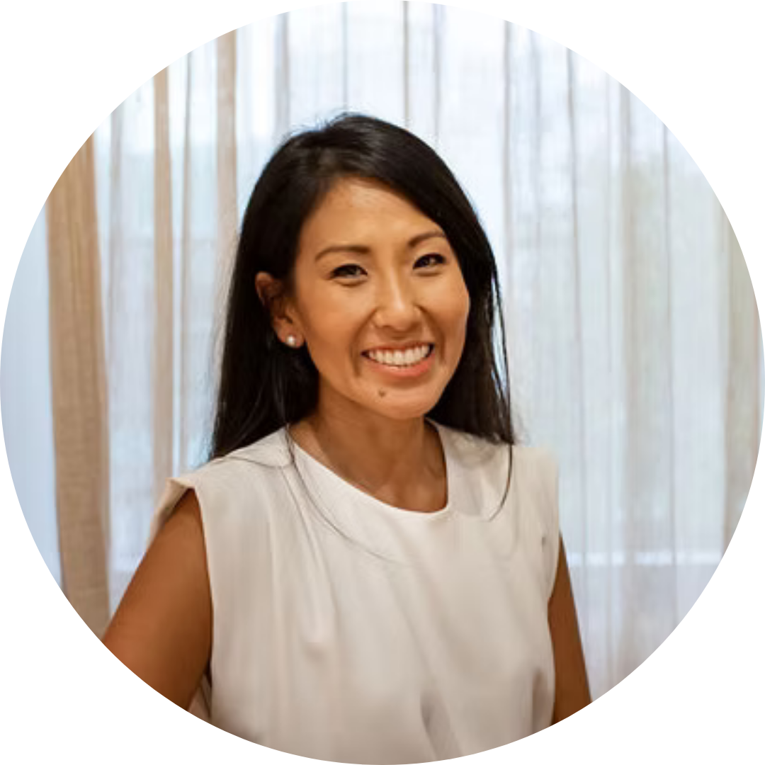 A man in a blue shirt is standing with his hands on his hips and smiling.