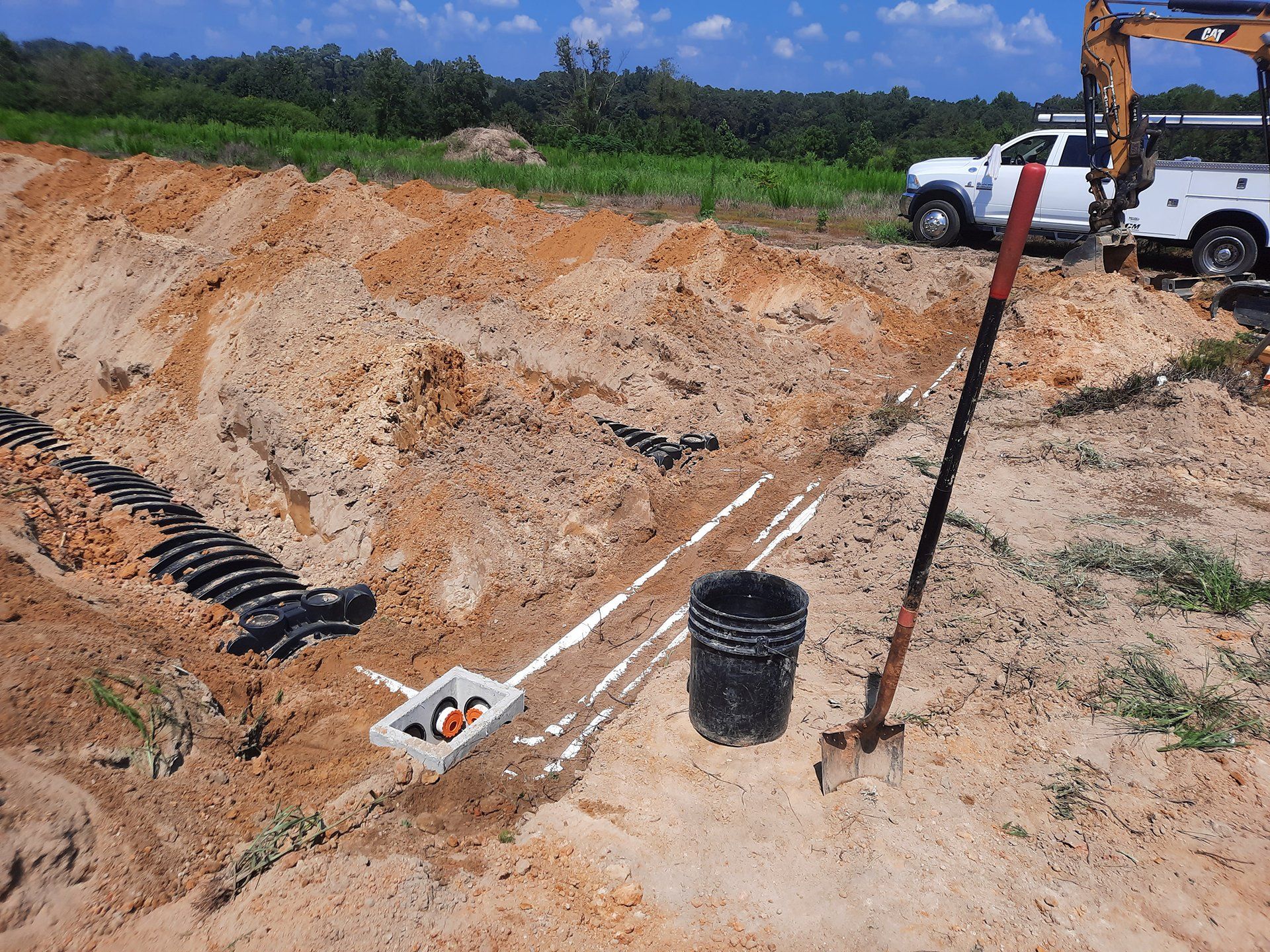 Trench excavation site with black pipes, tools, and a utility truck on sandy ground under a blue sky