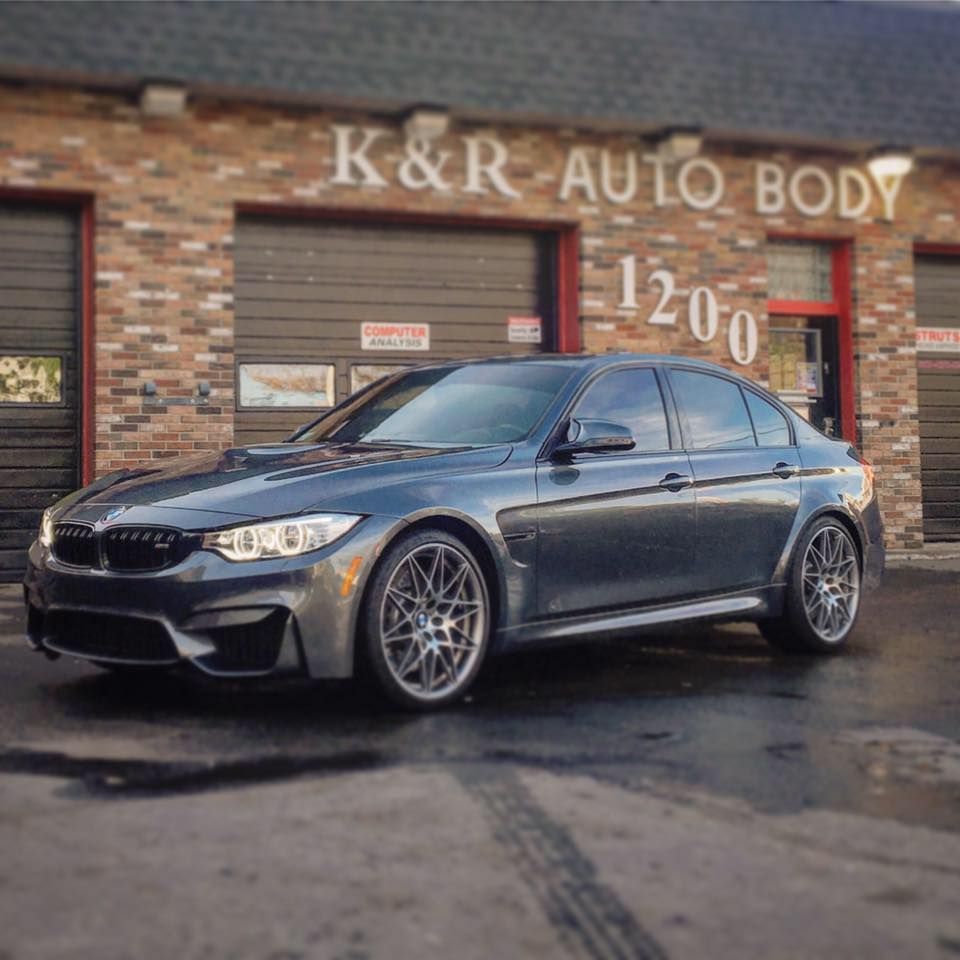 Gray BMW M3 sedan parked in front of K&R Auto Body shop with a brick exterior.