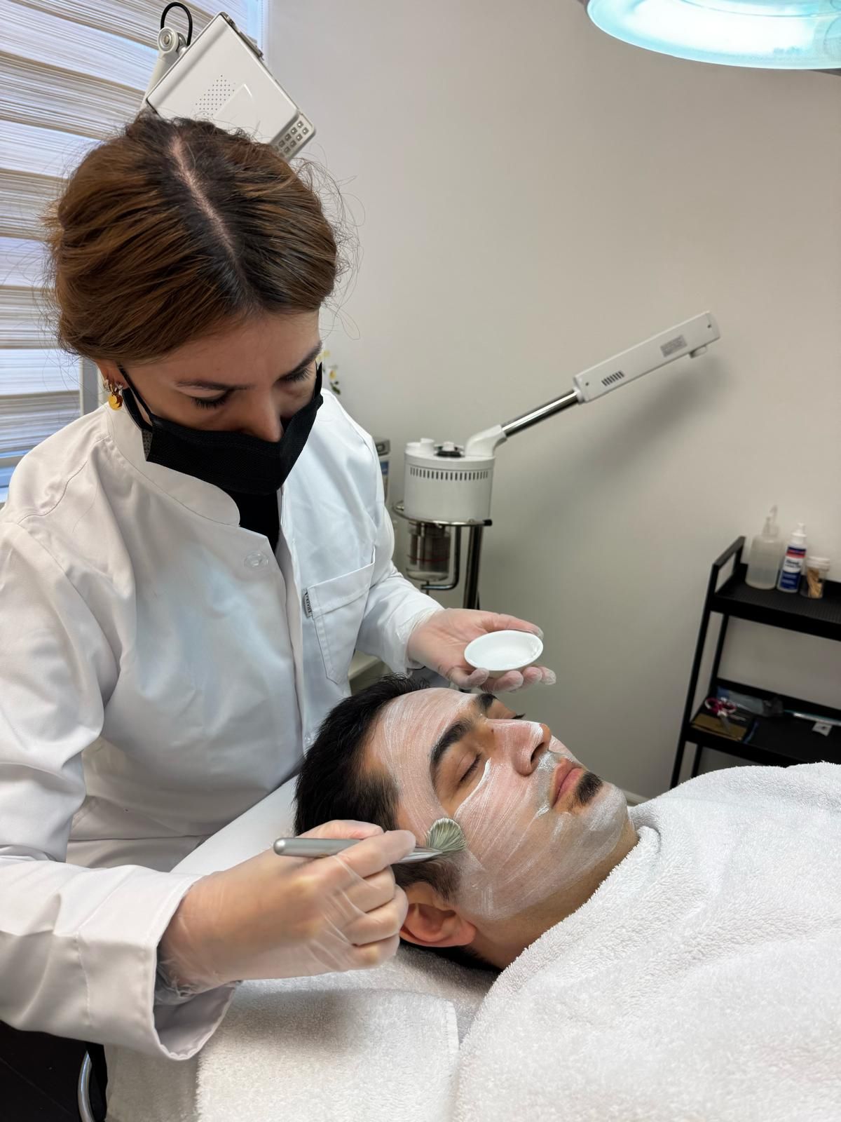 Facial treatment in a spa, with a technician applying cream to a reclining client