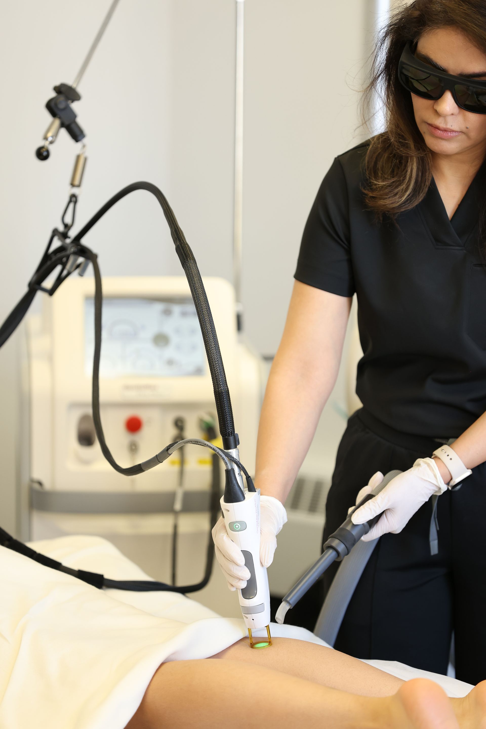 Clinician in black top uses a handheld laser device on a patient’s skin in a medical treatment room