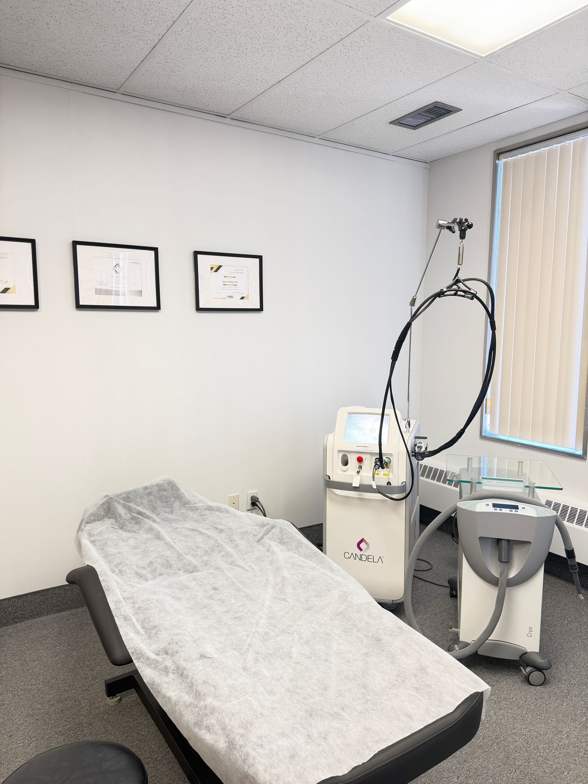 Exam room with treatment table, wall charts, and medical equipment beside a window