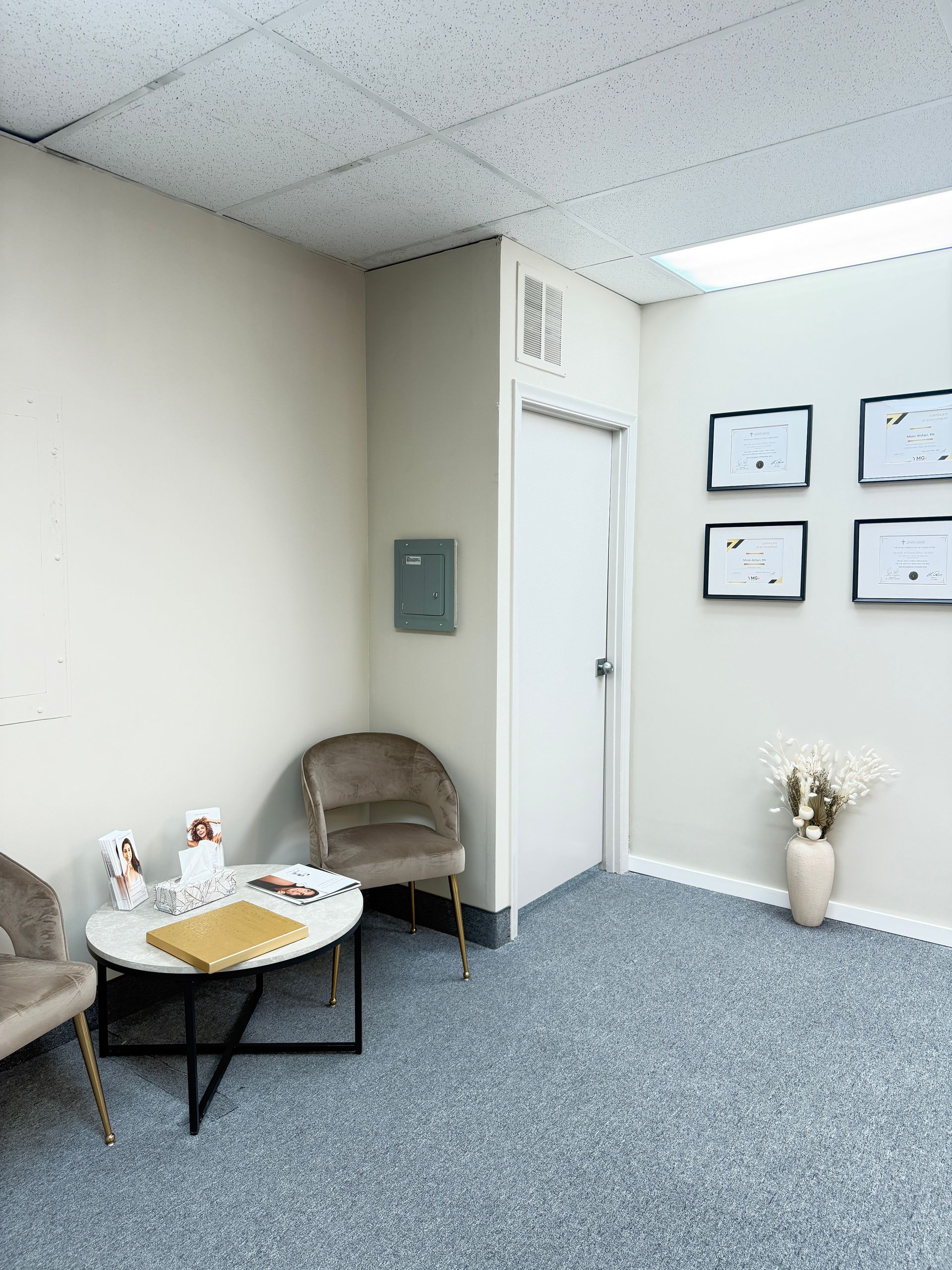 Quiet waiting room with beige chairs, small table, wall art, and carpeted floor.