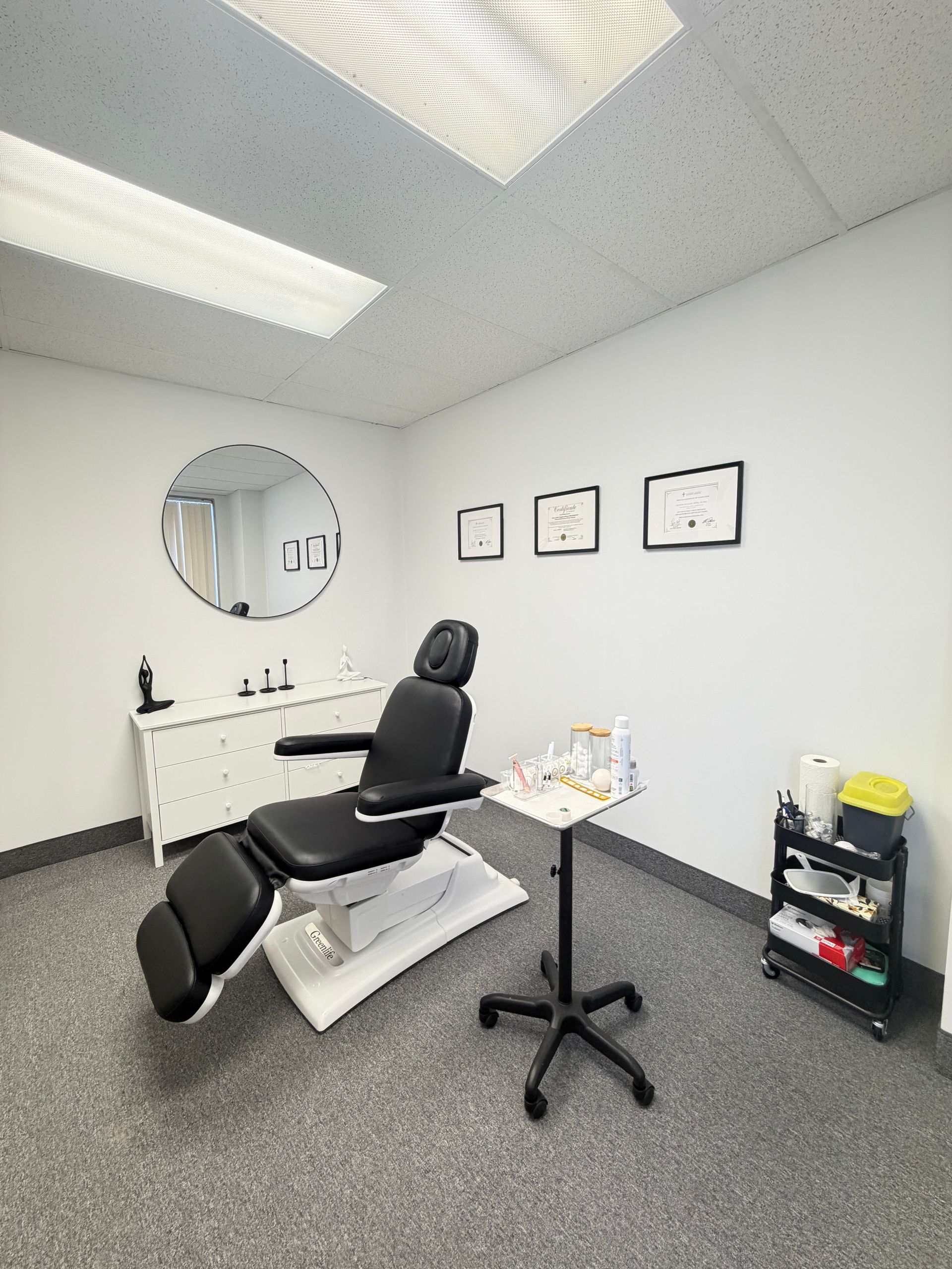 Dental exam room with black reclining chair, sink, mirror, wall frames, and small cart