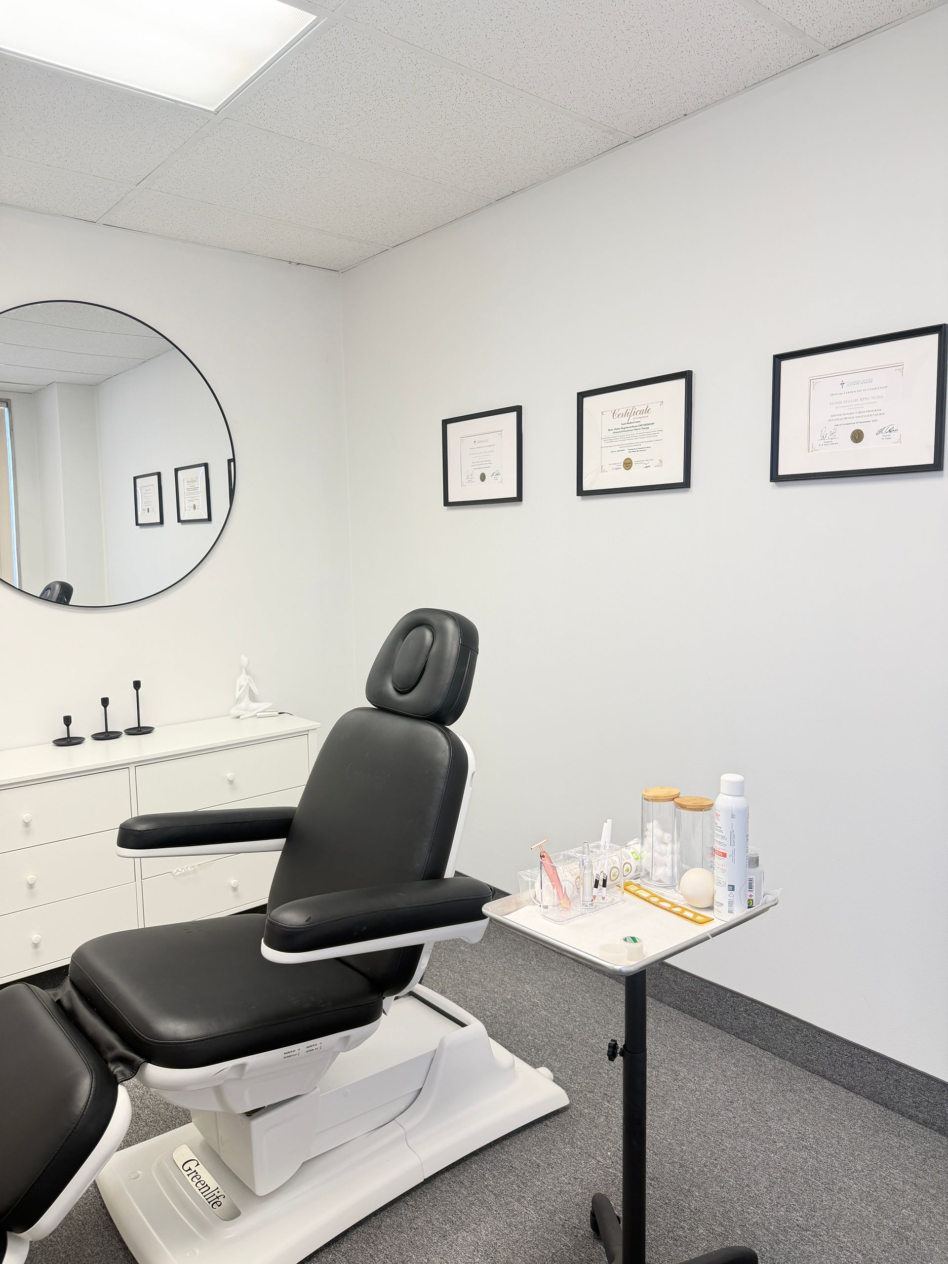 Exam room with black treatment chair, round mirror, and framed wall art on white walls