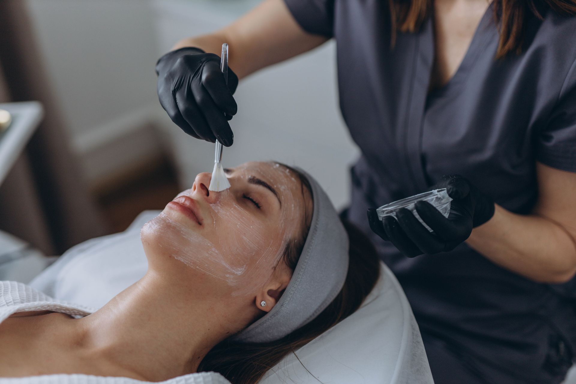 Facial treatment in progress, with a technician applying serum to a client’s face in a spa setting