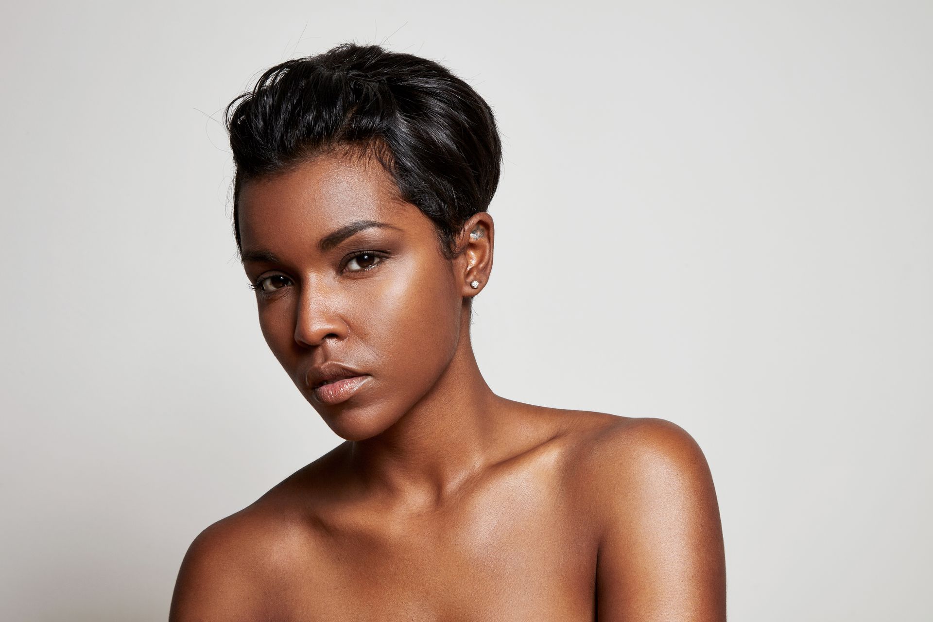 Portrait of a person with short dark hair against a light gray background, looking at the camera with a neutral expression