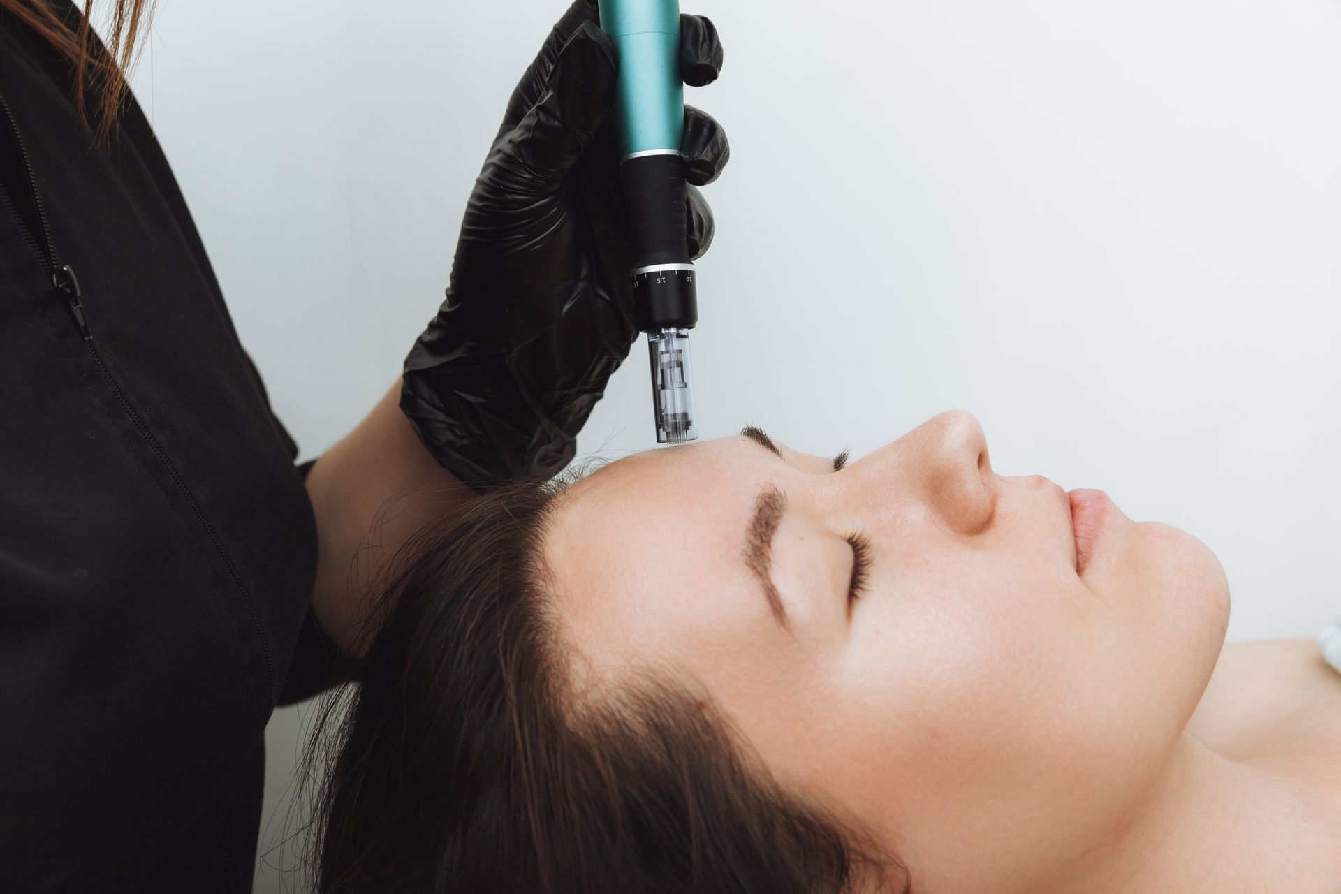 Gloved hand using a facial treatment tool on a woman lying down with eyes closed