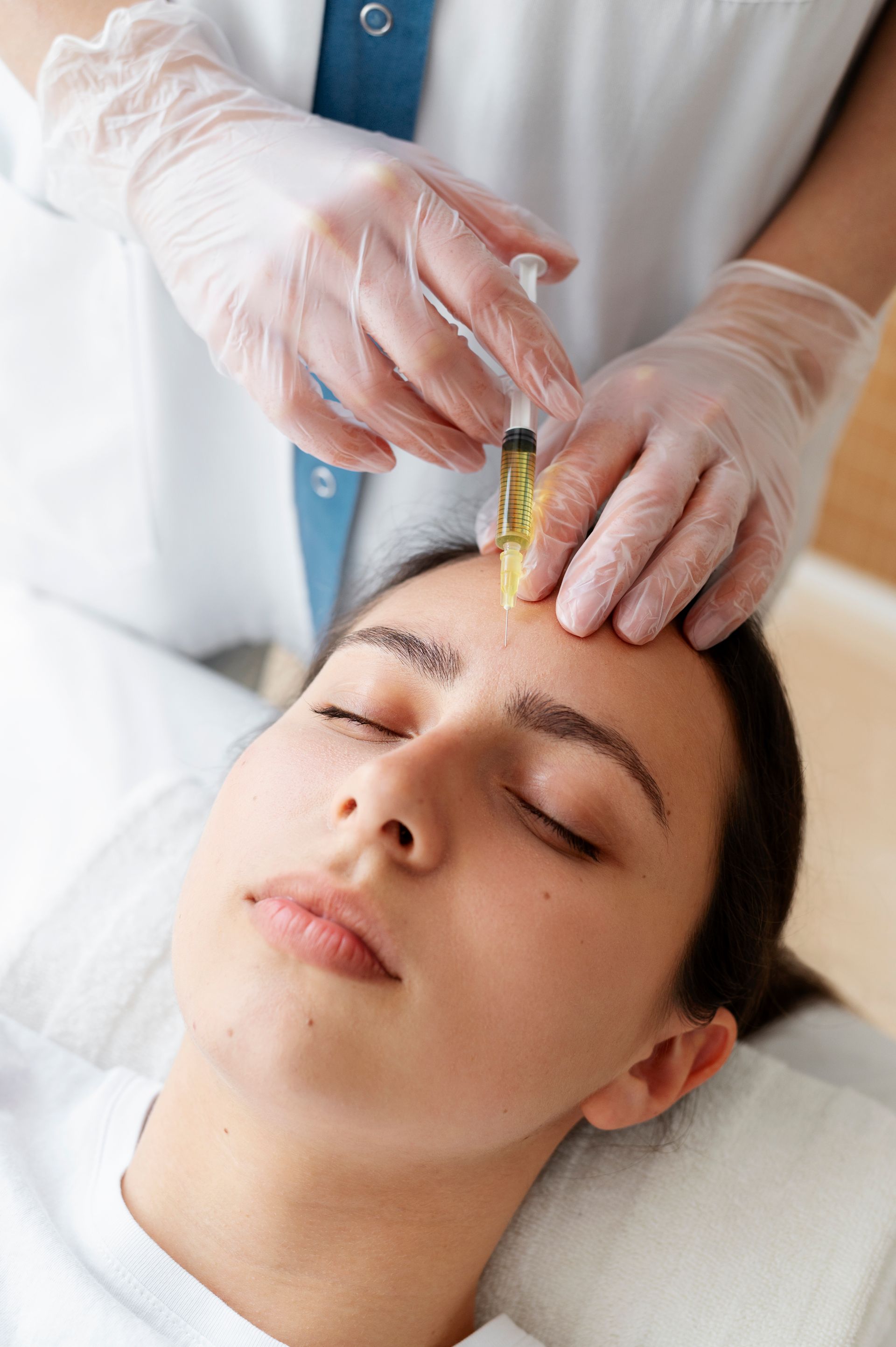 Esthetician applying a facial treatment with a syringe-like tool to a client’s forehead