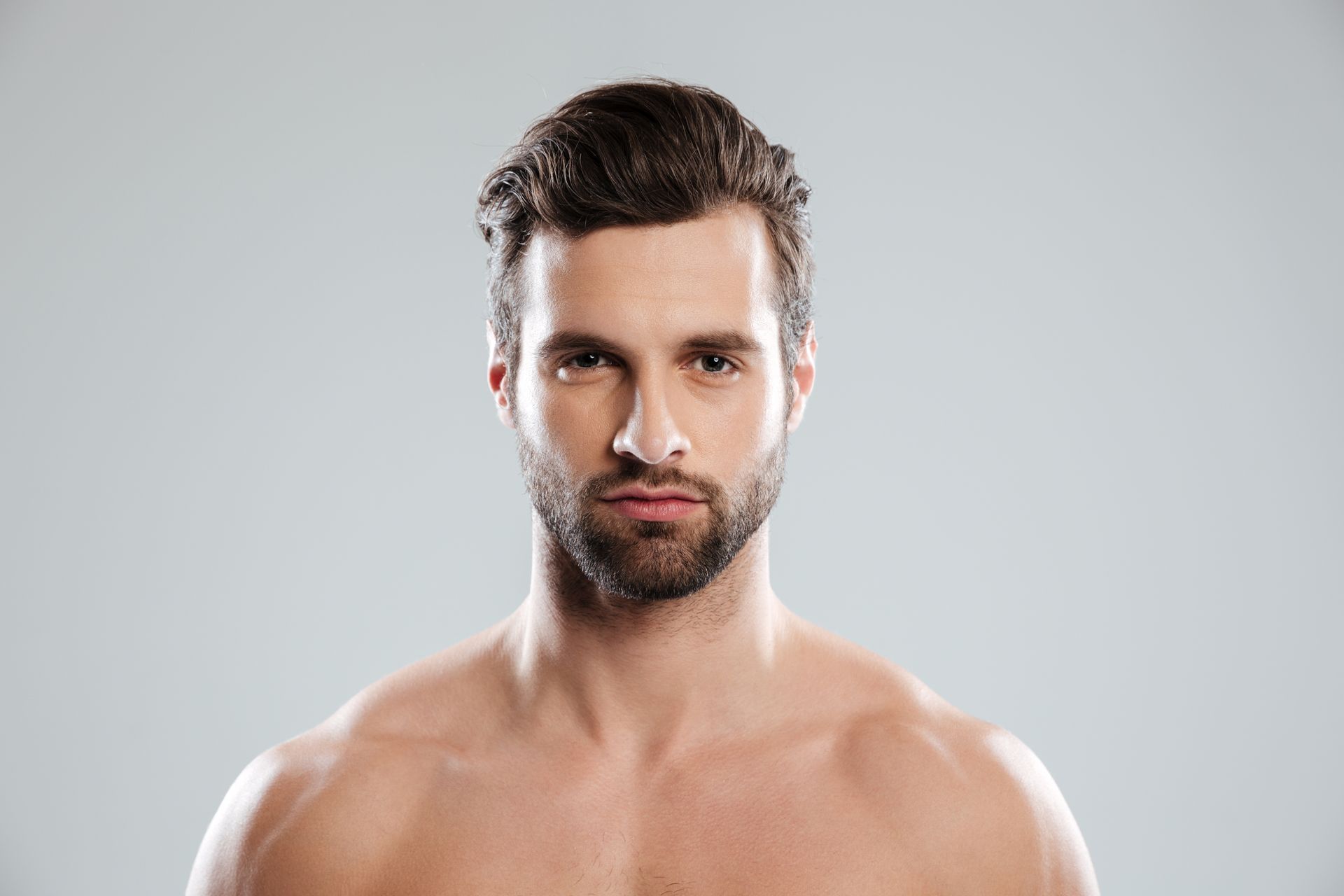 Portrait of a shirtless man with dark hair and beard against a light gray background