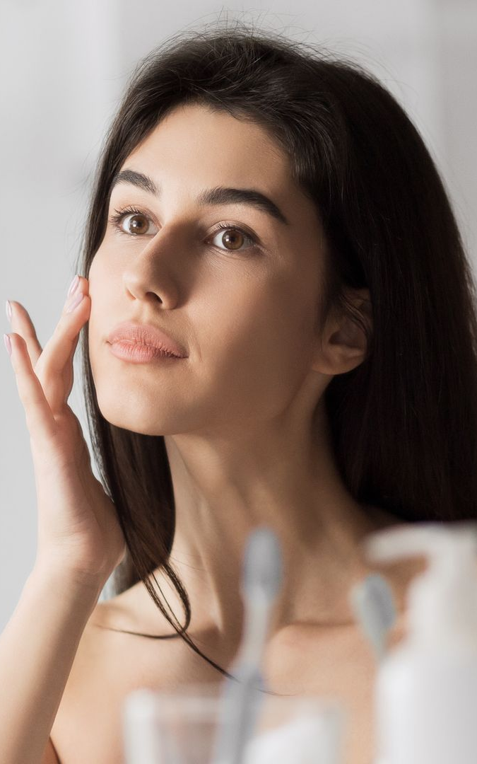 Woman applying skincare cream to her face in a softly lit bathroom