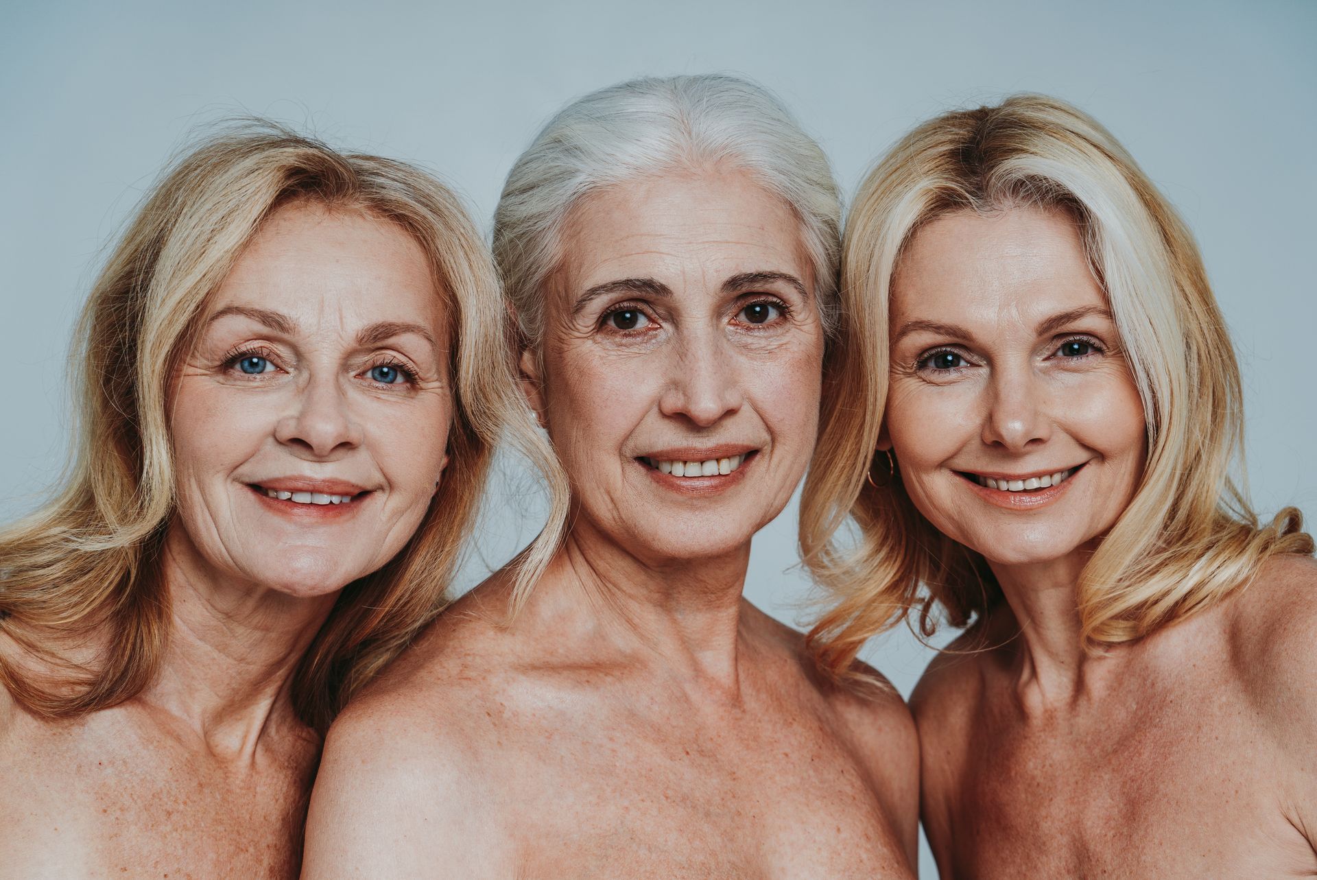 Three smiling women posing closely together against a light background