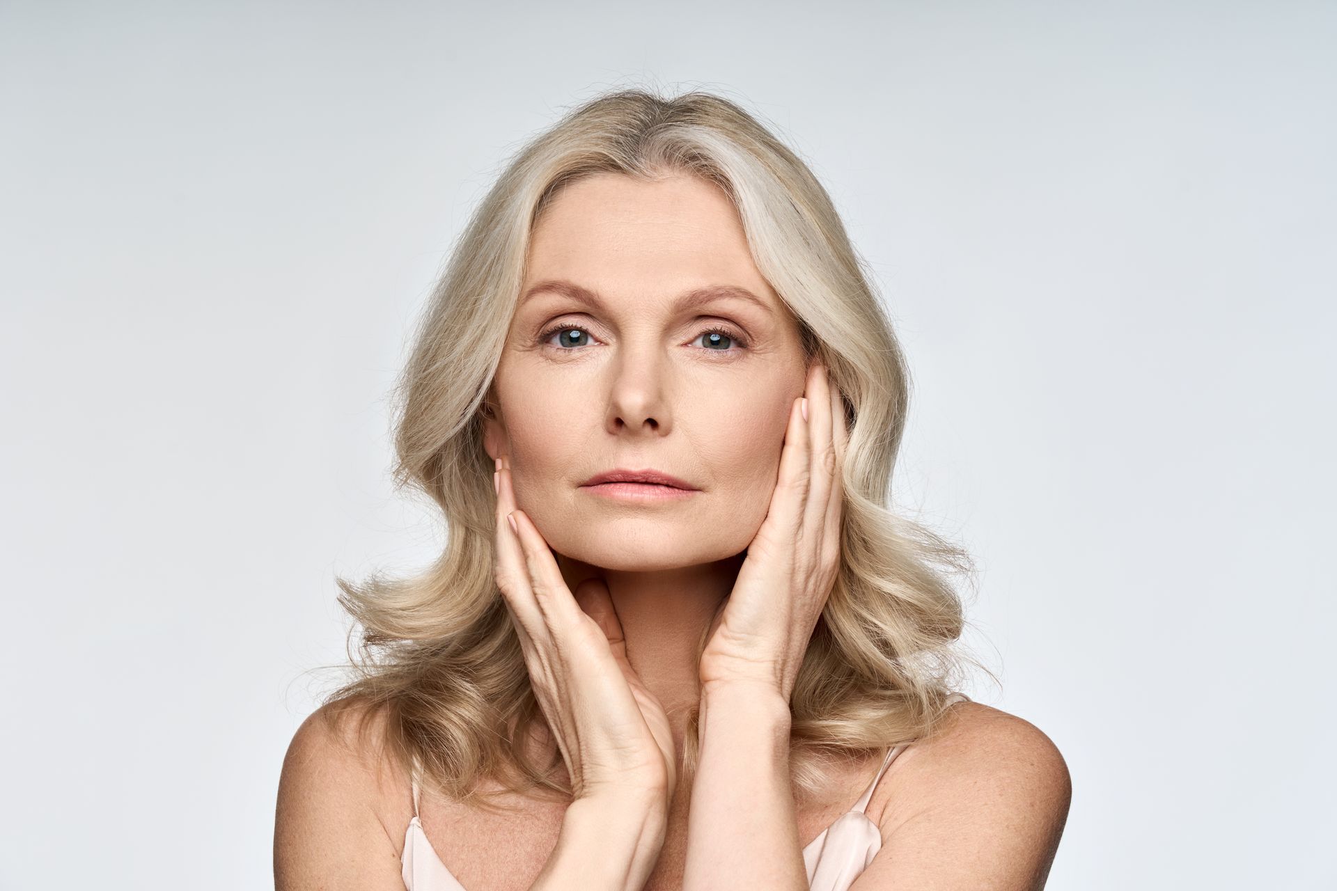 Portrait of a blonde woman with hands on her face against a light gray background